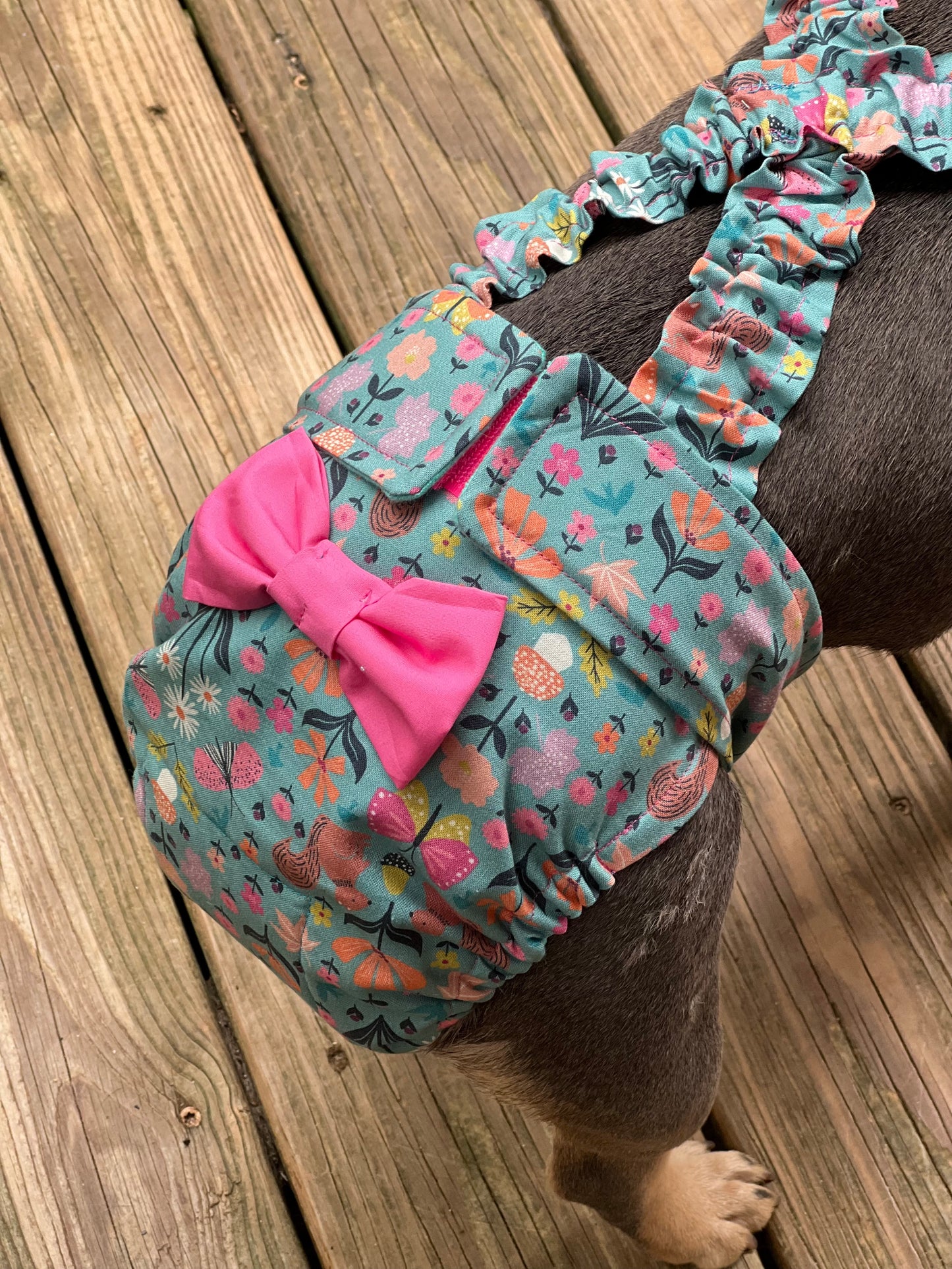 Dog wearing a floral diaper with a pink bow on a wooden floor