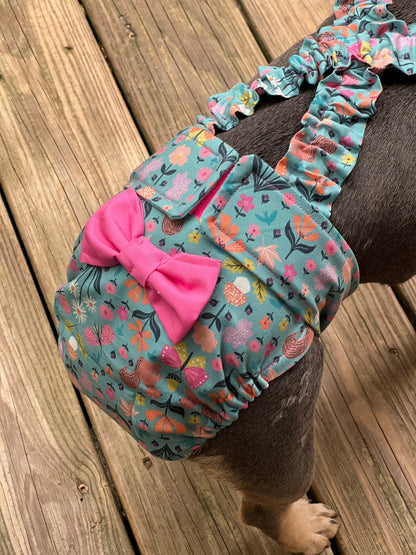 Dog wearing a floral diaper with a pink bow on a wooden floor